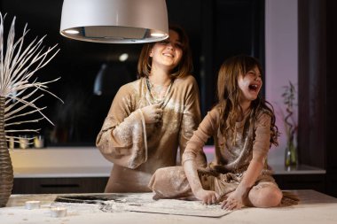 Kız ve anne mutfakta un kullanarak yemek pişiriyor, kız her yerinde unla oynuyor.