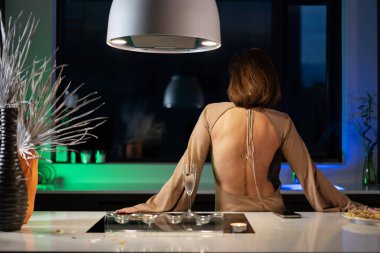 Bir kız güzel bir gece elbisesiyle mutfakta duruyor ve şampanya içiyor. Randevu bekliyor.