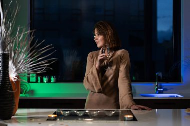 Bir kız güzel bir gece elbisesiyle mutfakta duruyor ve şampanya içiyor. Randevu bekliyor.