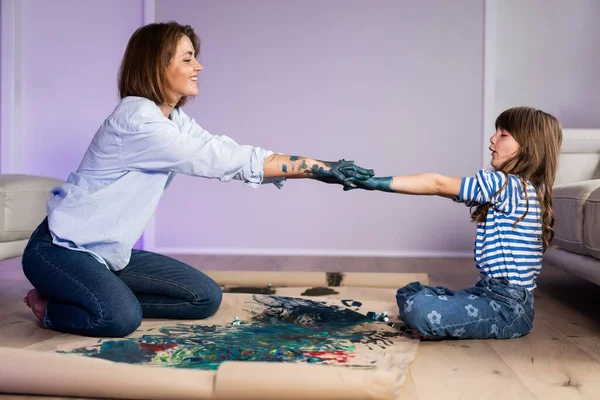 ママと娘は両手で油絵と段ボールの床に一緒にペイントします ロイヤリティフリーのストック写真