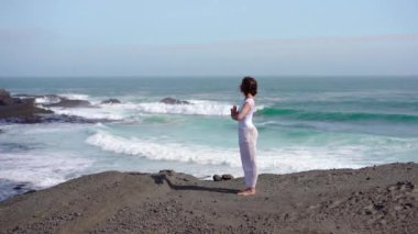 Okyanus kıyısındaki bir kayanın üstünde yoga yapan bir kız, gün batımında İzlanda 'da bir dronun manzarası.