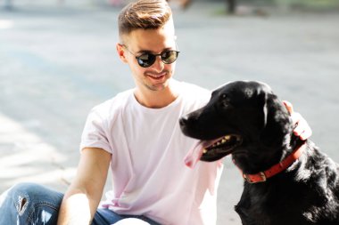 Güneş gözlüklü adam gün batımında sonbahar parkında köpeğine sarılır.