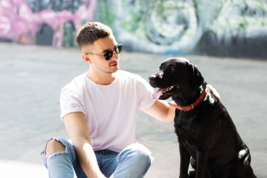 Güneş gözlüklü adam gün batımında sonbahar parkında köpeğine sarılır.