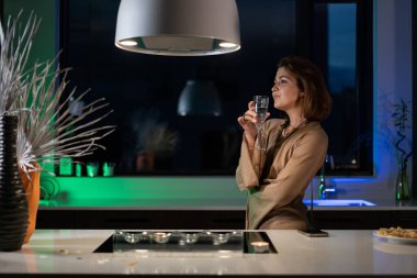 Bir kız güzel bir gece elbisesiyle mutfakta duruyor ve şampanya içiyor. Randevu bekliyor.