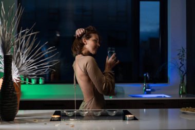 Bir kız güzel bir gece elbisesiyle mutfakta duruyor ve şampanya içiyor. Randevu bekliyor.