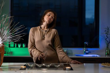 Bir kız güzel bir gece elbisesiyle mutfakta duruyor ve şampanya içiyor. Randevu bekliyor.