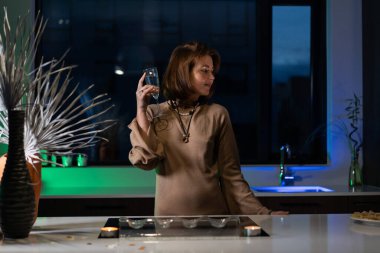 Bir kız güzel bir gece elbisesiyle mutfakta duruyor ve şampanya içiyor. Randevu bekliyor.