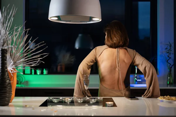 Bir kız güzel bir gece elbisesiyle mutfakta duruyor ve şampanya içiyor. Randevu bekliyor.