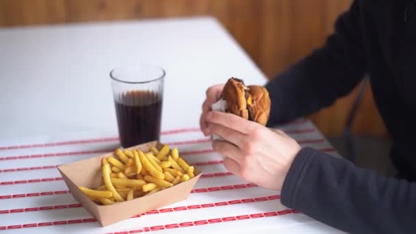 おいしいジューシーなハンバーガーを楽しんでレストランでハンバーガーを食べる男とフランスのフライドポテト — ストック動画