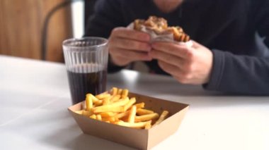 Lokantada hamburger yiyen adam lezzetli hamburgerin ve patates kızartmasının tadını çıkarıyor.