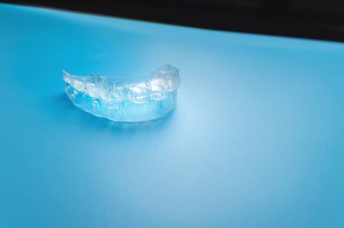 A transparent aligner lies on a bright background. No people.