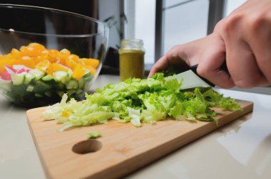The cook cuts the salad with a knife on the table at home. The process of cutting and cooking food in the kitchen close-up.