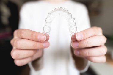 Close-up of a womans hand holding invisible aligners for whitening and straightening teeth on a blurred background. Orthodontic treatment after braces. Dental health.