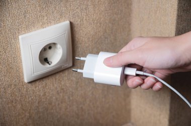 Womans hand turns on, turns off the charger in the electrical socket on the wall in the house, close-up.