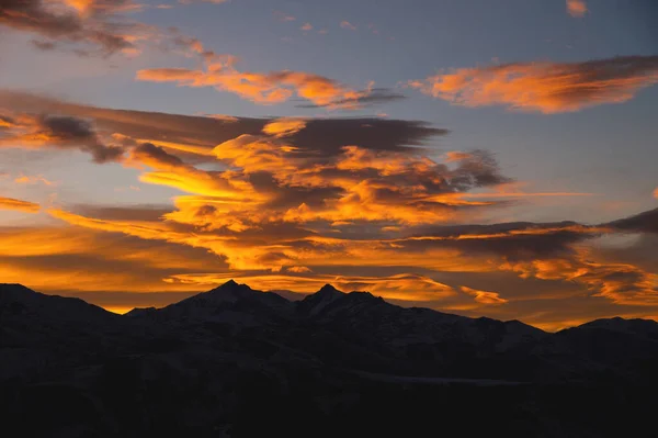 Sunset in the mountains, mountain silhouette against a cloudy sky in orange colors.