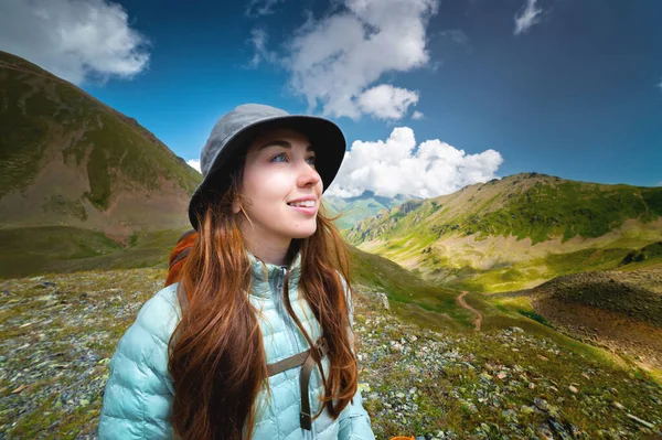 Portrait of a smiling woman resting during a mountain hike. A woman with a backpack enjoys the view while standing in the mountains. Happy tourist.