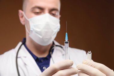 Doktor üniformalı yakışıklı adam elinde şırınga ve ampul tutuyor..