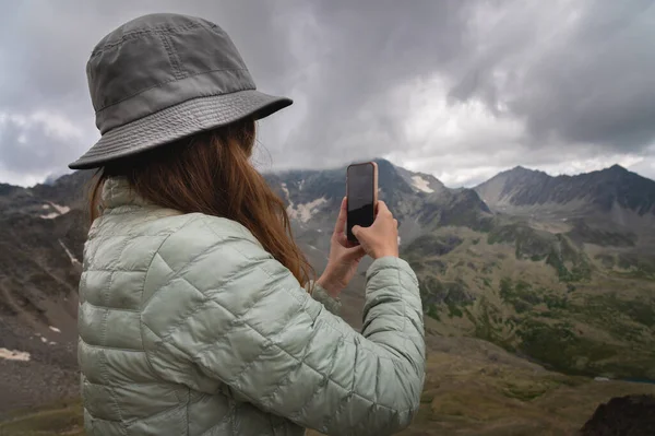 stock image A woman takes a picture on the phone while standing on top of a hill. Portrait of a tourist in the mountains.