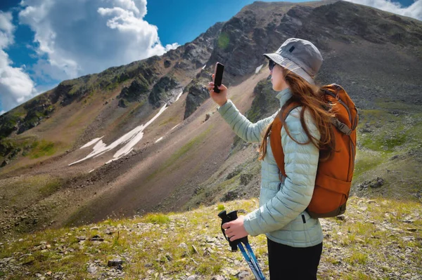 Side view of female blogger taking selfie on smartphone while hiking, discovering wild lands on vacation, wanderlust girl using phone to take photo while standing on rock, breathtaking scenery.