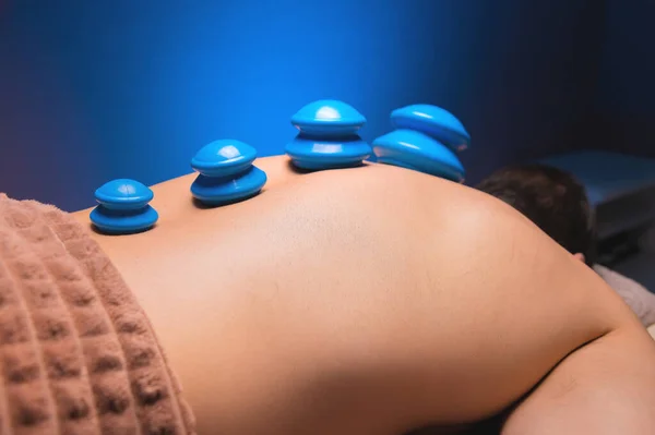 Cupping massage in general. Vacuum rubber cups for back massage for a man. Massage with vacuum cups. Cupping treatments for back pain relief. A white male lies face down with suction cups mounted on