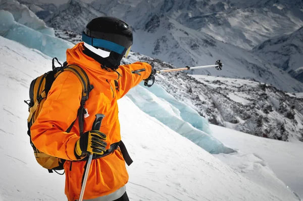 赤いジャケット ヘルメット マスクのプロのスキーヤーアスリートは 氷河や壮大な山々を背景に斜面に立っています スキー ポールを山の中で指す Freeride Concept — ストック写真
