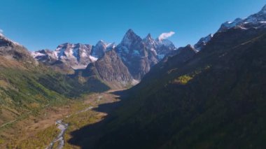 Yüksek dağları ve altında bir nehir bulunan dağ vadisinin havadan görünüşü. Ulaşılması zor doğal yerlerde Alp turizmi. Güneşli bir gün. Bakire doğa.