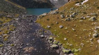 Bir dağ gölünün önündeki dağ yolunda bir çift genç adam ve kadın havadan çekim yapıyorlar. Aile yürüyüşleri ve tatiller dağlarda. hava görünümü.