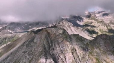 Kafkasya 'nın tepelerindeki bilinmeyen kayalık bir dağın sinematik hava aracı görüntüsü. Güneşli bir günde yüksek dağ gölleri ve uçurumlarla çevrili. Bulut oluşumları