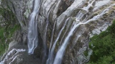 Güneşli bir günde dağların yükseklerinde bir buzul şelalesinin havadan görünüşü. 4k yüksekliğinde bir şelaleye yaklaş.