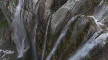 Buzuldan kayaların üzerinden akan dağ şelaleleri ile hava manzarası yakın uçuştadır. Yeşil bir dağ geçidine düşen su. Üç eksende hareket.
