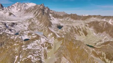 Yazın karla kaplı dağların havadan görünüşü. Dağlarda güneşli bir gün. Dağların tepesindeki kayalar. Dağlarda insanlar olmadan havadan ateş edildi..