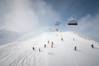 Kayak merkezinin panoraması, yamaç, asansördeki insanlar, kayakçılar ve beyaz karlı kayakçılar. Güneşli bir tatil günü, üst manzara.