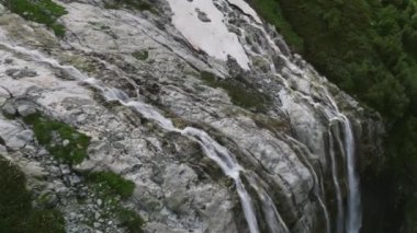 Güneşli bir günde dağların yükseklerinde bir buzul şelalesinin havadan görünüşü. 4k yüksekliğinde bir şelaleye yaklaş.