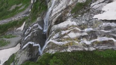 Güzel bir şelalenin havadan çekilmiş fotoğrafı. Kamera aşağıya bakıyor. Kafkasların yüksek dağlarında, sarp kayalıklardan düşen su damlaları..