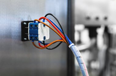 Çevreleyiciler ve kontrol kablolarıyla çevrili bir üretim hattında elektrik kontrol kabininde bir sürü anahtar var..