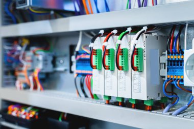 Çevreleyiciler ve kontrol kablolarıyla çevrili bir üretim hattında elektrik kontrol kabininde bir sürü anahtar var..