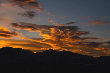 Dağ tepelerinde renkli günbatımı. Dağların siyah silueti resimsel parlaklıktan görülebiliyor..