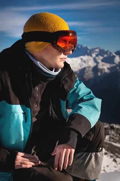 斯基人坐在山顶上 在雪山里 一个阳光灿烂的日子 年轻人蹲在温暖的衣服里 — 图库照片