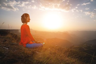 Bir kadın yoga yapıyor ve bir dağda meditasyon yapıyor. Şafak vakti güneşin altında yeni bir günün enerjisini alan bir Yogi 'nin yan görüntüsü..