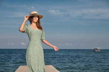 Yazın açık havada gülümseyen genç kadın, okyanus ya da deniz kıyısında yeşil elbiseli, güneşli moda portresi..