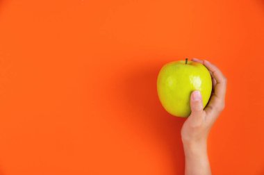 Kadınların iki eli parlak kırmızı arka planda bir elmayı tutuyor. Eller ve taze meyveler, üst manzara. Düz yatak, diyet ve sağlıklı beslenme konsepti.