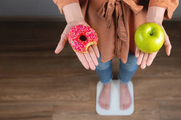 여자가 그녀의 칼로리 디저트와 사과와 도넛을 개념을 어렵습니다 녹색을 여자와 — 스톡 사진