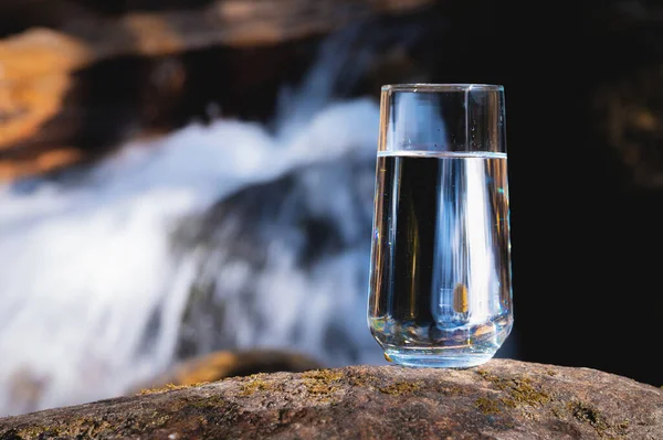 Natural water in a glass. Pure water in a transparent glass against the backdrop of a mountain river in the background. Healthy food and clean natural water.