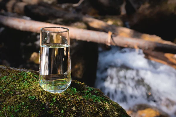 A glass of water, purified fresh drinking water on a stone with grass and moss outdoors. Nature in the background.