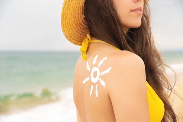 黄色い水着の魅力的な若い白人女性は 太陽の形で彼女の肩に日焼け止めをしています 海の夏の太陽の健康な皮 — ストック写真