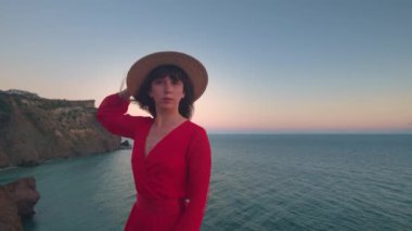 Gerçek zamanlı. Nazik, oyuncu bir kız, sakin ve güzel bir okyanusun önünde dururken baştan çıkarıcı bir gülümsemeyle kameraya bakar. Hasır şapkalı çekici kıvırcık kadın kameranın önünde flört ediyor.