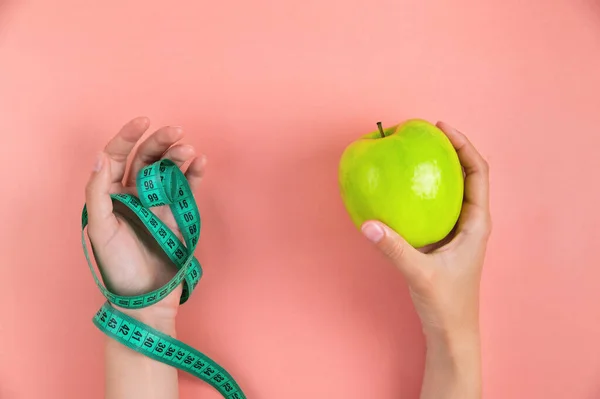 女性の片手には緑のリンゴがあり もう片手はピンクの背景に測定テープを持っています 減量とダイエットのコンセプト — ストック写真