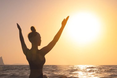 Özgür mutlu kadın ellerini kaldırır ve güneşe bakar, arkadan bakar. Arka planda, şafakta, yoga ya da meditasyon sırasında güneşi selamlıyorum..