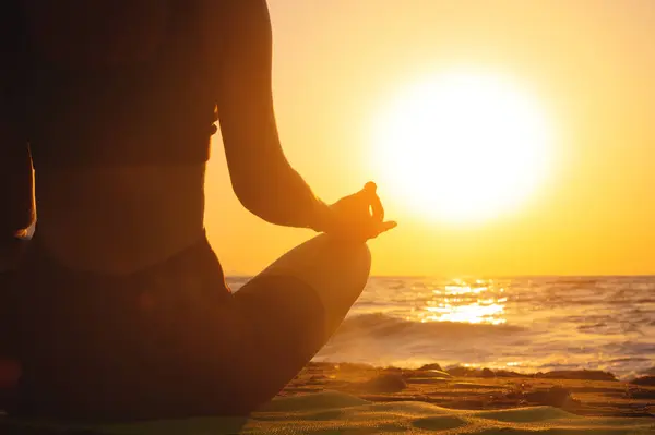 Close-up womans hand practicing yoga silhouette, meditation in lotus position on the beach, feel so comfortable and relax on vacation with golden light, healthy concept.