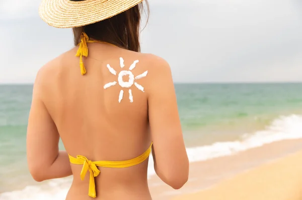 Sun protection. A beautiful, unrecognizable girl wears sunscreen on her tanned shoulder in the shape of a sun. Skin care, young woman in a straw hat and swimsuit stands with her back to the camera at
